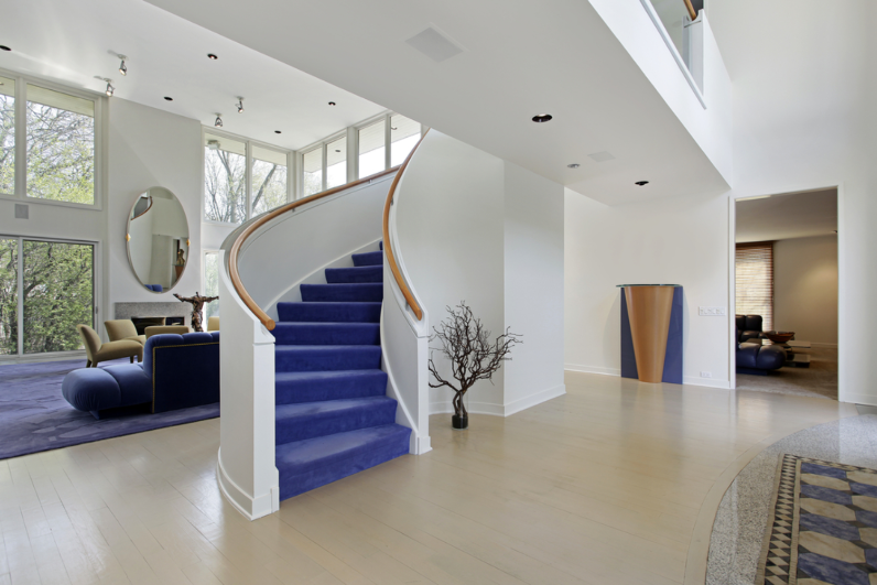 Tầng trệt ngôi nhà với các bức tường trắng, chính giữa là cầu thang có các bậc thang màu tím.