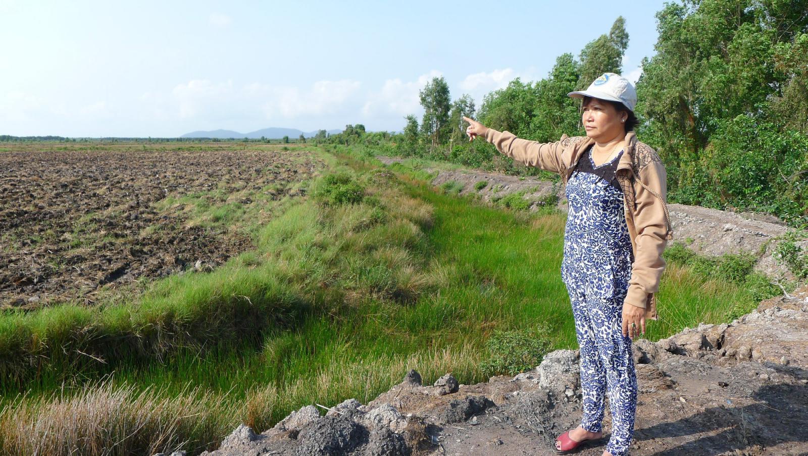 một người phụ nữ đứng chỉ tay ra khu đất trống